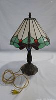 Full view of Tiffany style stained glass table lamp with metal base and cord attached.