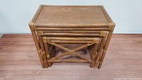 View of three bamboo nesting tables stacked together showing front and side frames with cross-bracing.