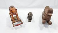 Three items shown together: a wooden rocking pig on curved rocker base, a bronze cat statue, and a wooden duck rocker on wheels, all photographed on white background.