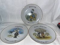 Three Holly Hobbie decorative plates arranged side by side showing each with a gold rim and vintage graphics.