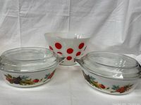 Photo of three milk glass bowls: one white opaque Fire King bowl with red polka dots and two clear glass JAJ England bowls with floral and fruit decoration and lids.