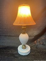 Full view of milk glass hobnail base table lamp illuminated, showing amber glow underneath pink glass shade.