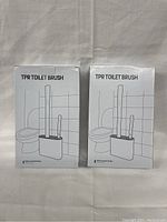 Photo of two boxed toilet brush sets side by side showing front of boxes with 'TPR Toilet Brush' and a simple drawing of the product.