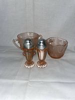 Pink Depression Glass Creamer, Sugar Bowl, and Salt and Pepper Shakers on plain cloth background.