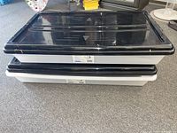 Two stacked underbed storage containers showing black lids and white bases, placed on carpet.