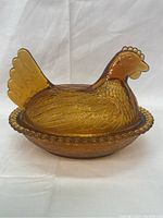 Front-side view of vintage amber gold Indiana Glass candy dish shaped like a hen sitting on a beaded nest base.