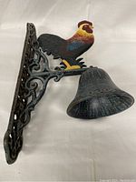 Side view of vintage cast iron rooster bell mounted on ornate bracket, showing bell and rooster figure.