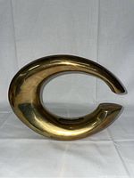 Front view of the brass 'C' shaped vintage Ikebana vase showing the smooth, shiny brass surface and sculptural form.