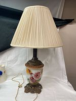 Full view of vintage milk glass table lamp showing pleated fabric shade, painted milk glass body and leaf-patterned brass base