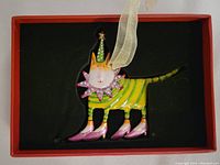 Metal jeweled cat ornament with green and yellow stripes, pink shoes, a pink jeweled collar, and green star-topped hat in black box