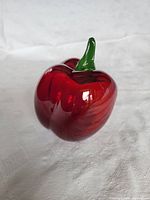 Photo showing front side of the blown glass red pepper ornament with green stem on a white cloth background.