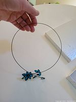Blue flower necklace held by hand showing wire and flower detail.
