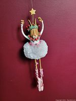 Ornament displayed upright against a red background showing full figure in tutu and ballet slippers with star on head.