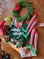 Photo showing the elf legs, Grinch arm, green holiday wreath, candle holder with antlers, two decorative sleighs, gift bags, artificial greenery, red berry decoration, Christmas crackers, and cards.