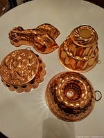 Top-view photo of four copper-colored decorative molds arranged on a white round table, showing detailed patterns and shapes for identification.