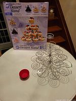 Photo of Wilton Cupcakes 'N More Dessert Stand with box, metal wire spiral design and some red silicone muffin cups, showing item and packaging.