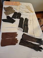 Gloves arranged on a white surface showing different colors and materials including leather and cloth, long and short styles, and some gloves with visible linings.