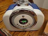 Front angled view showing the digital control panel with time display and multiple control buttons. The humidifier is white and blue with chrome accents.