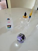 Lot items on white glossy tabletop: purple egg-shaped signed perfume bottle, glass inkwell, and glass fountain pen with amber nib