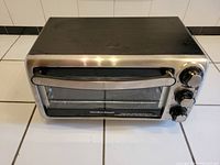 Front and top view of Hamilton Beach stainless steel toaster oven showing three rotary dials, handle, and branding.