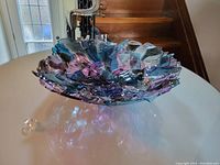 Colored glass art bowl displayed on table showing fused glass pieces in blues, purple, pink and green hues