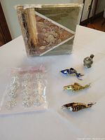 Overview photo showing all lot items including three metal/enamel painted fish, the jeweled bird trinket box, sparkly fashion pins sealed in packaging, and the natural fiber photo album wrapped in plastic