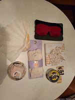 Lot arranged flat on white surface showing shell soap dish, white night cap in packaging, pink eye masks, white spa headband, lotion candle tin, and bath bomb