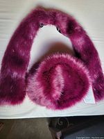 Fuzzy burgundy hat and matching scarf laid out flat on a white surface. Shows the texture and color of the items clearly with tags visible on the scarf.