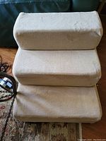 Front view of the three-step beige pet stairs showing soft fabric covering and rounded edges on each step.