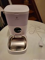 Front view of the Petlibro pet feeder with stainless steel food bowl and power cord placed on a white table.