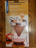 Box with product details showing KitchenValue rotary food press with stand and pestle, new in box packaging.