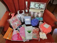 Full view of spa and beauty lot including bottles, bath salts, bath bombs, poufs, facial masks, and boxes on a red chair.