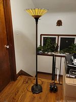 Full view of the floor lamp showing stained glass style shade, straight pole and ornate base against wall