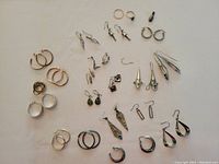 Full view of lot with all earrings and ring arranged on flat surface, showing variety of metal finishes and styles.