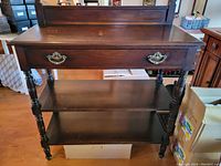 Front view of the vintage solid wood sideboard showing drawer, shelves, and turned legs.
