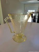 Front and side view of vintage yellow depression glass pitcher showing floral embossed pattern, spout, angular handle, and pedestal base.