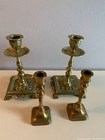 Two pairs of brass candleholders displayed together, showing size difference and general condition.