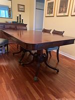 Full view of wooden rectangular dining table with two pedestal bases and chairs around it.