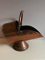 Side view of copper coal scuttle showing the curved handle and smooth rounded shape.