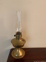 Full view of the brass hurricane lamp showing the lamp standing on a surface with clear glass chimney extending up.