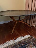 Full view of round brass tabletop with wooden base and four curved legs, showing overall shape and condition.
