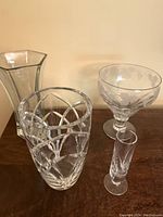 Four vases displayed together on wooden surface including clear glass hexagonal vase, two cut crystal vases, and a smaller clear vase.