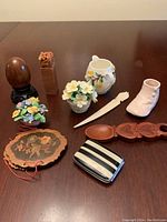 Full view of all items including ceramic florals, wooden spoon, letter opener, ceramic shoe and jug, striped box, and carved wooden box.
