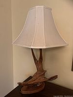 Full view of the lamp showing the white fabric lampshade and the driftwood base on a wooden surface.