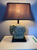Full front view of the lamp showing the elephant base and the textured rectangular lampshade lit up.
