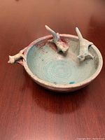Full view of ceramic bowl showing overall shape, glaze colors, and the three attached cat figures on rim.