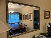 Full view of the mirror hanging on a wall, showing reflection of dining room with table, chairs, paintings and window