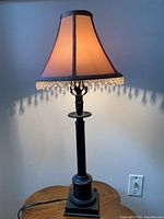 Full view of the metal base table lamp with fabric shade and crystal fringe lit to show lamp in working condition.