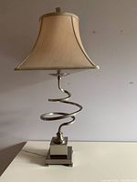 Front view of the metal table lamp with beige fabric lampshade and spiral metal body on a square base.