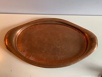 Top view of large oval copper tray showing patina, dents, and wear.